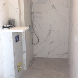 Bogdan - Nowoczesna łazienka w trakcie wykończenia, płytki imitujące marmur na ścianach i podłodze, widoczna kabina prysznicowa typu walk-in, narzędzia budowlane w rogu pomieszczenia.