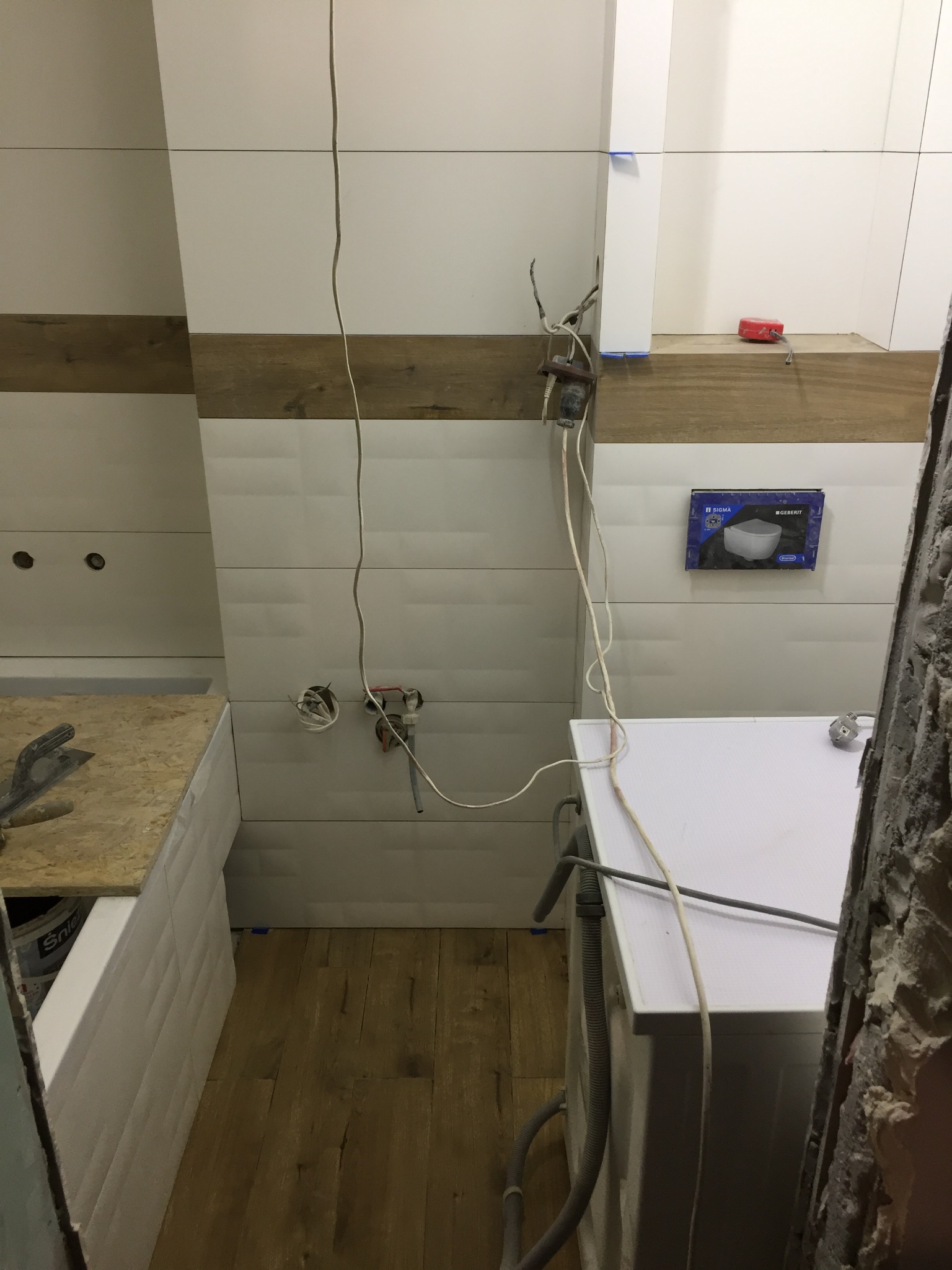 W Legnicy, w trakcie prac wykończeniowych w łazience: ułożone płytki ścienne z drewnianym dekorem, widoczne przewody elektryczne, przygotowane miejsce pod zabudowę umywalki i pralki, na podłodze...