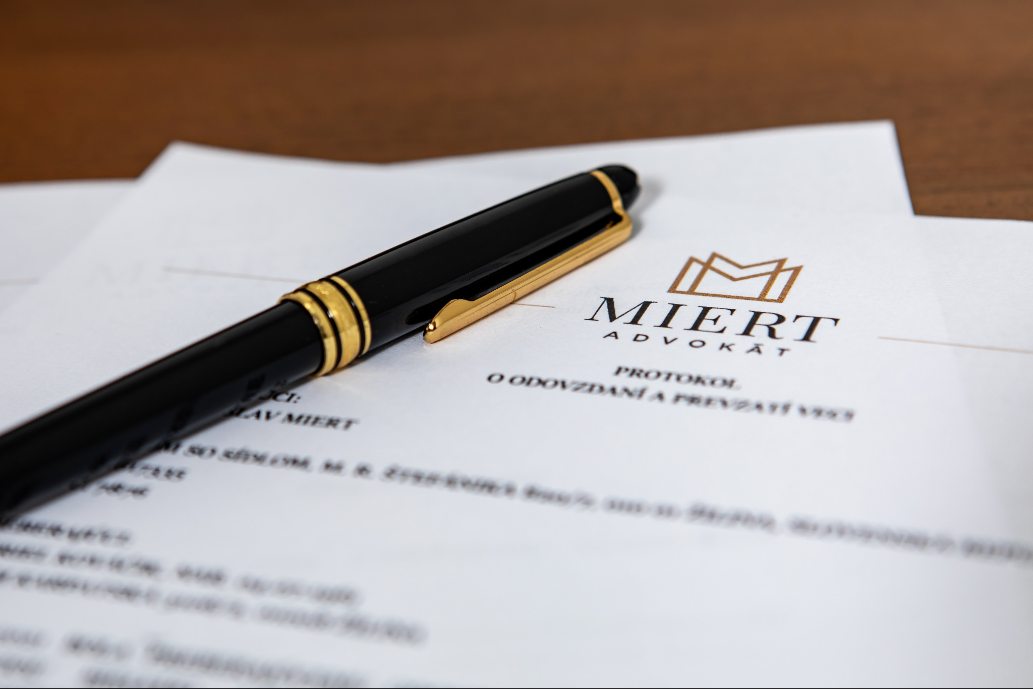 Czarno-złote pióro wieczne leżące na dokumentach z nagłówkiem 'MIERT ADVOKAT' na drewnianym biurku.