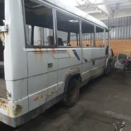 Zardzewiały, częściowo rozebrany autobus w warsztacie, widoczne ubytki karoserii i brak szyb, zdemontowane elementy wnętrza obok.