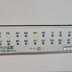 Panel sterowania inteligentnego domu z diodami LED oznaczonymi literami i cyframi, niektóre diody świecą na pomarańczowo, widoczny moduł zasilający Mean Well KNX-20E-640 oraz przyciski ON/OFF...