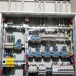 Rozdzielnia elektryczna z zamontowanymi zabezpieczeniami, bezpiecznikami i okablowaniem, widoczne przewody ułożone w korytkach.