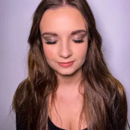 Portret kobiety z zamkniętymi oczami prezentujący makijaż oczu z brokatowymi cieniami i delikatny błyszczyk na ustach, na gładkim, jasnym tle.