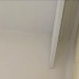 Fragment świeżo pomalowanego sufitu i ściany w jasnych, neutralnych odcieniach, widoczna listwa przypodłogowa przy suficie.