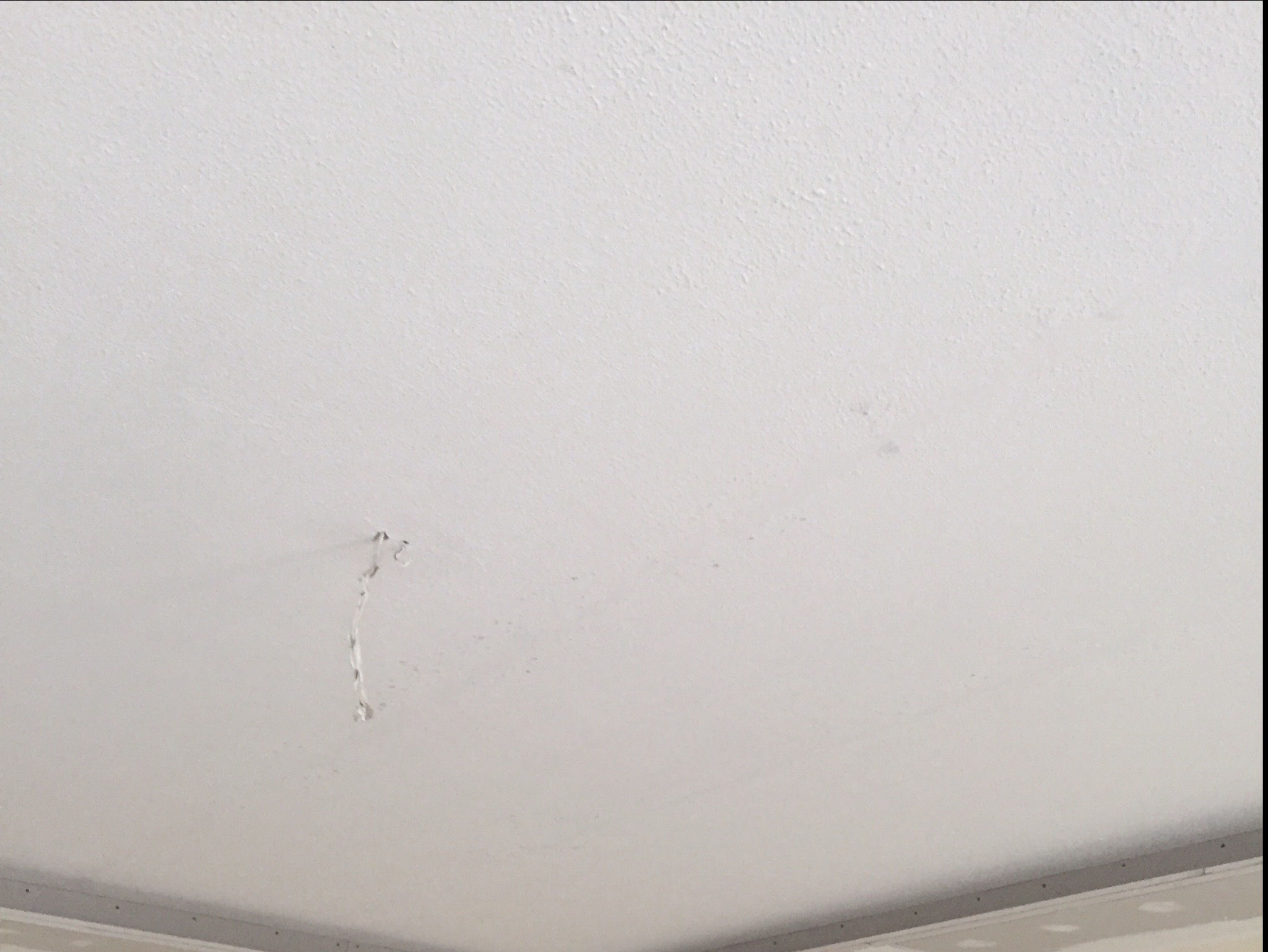 Biały, nierówny sufit z widocznymi śladami po mocowaniu, prawdopodobnie po demontażu lampy lub innego elementu, z fragmentem listwy przypodłogowej w dolnej części kadru.