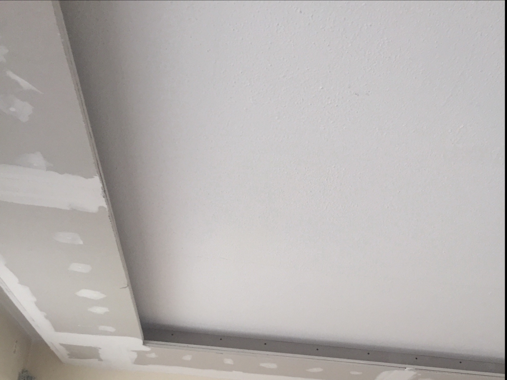 Fragment sufitu podwieszanego w trakcie montażu, widoczne profile i płyty gipsowo-kartonowe z widocznymi śladami szpachlowania.