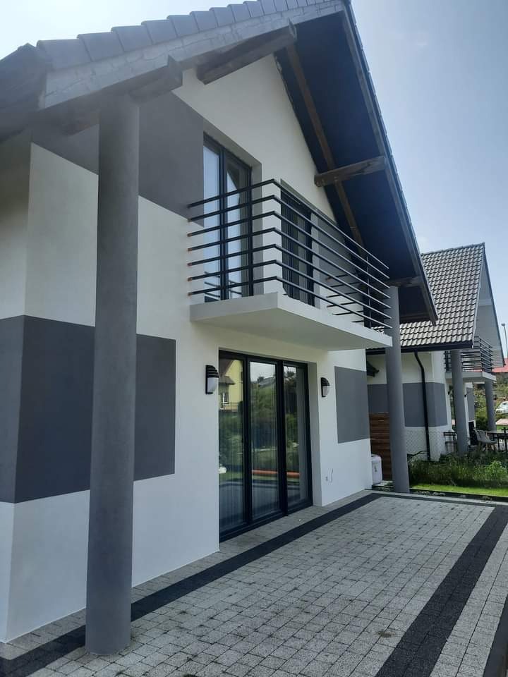 Nowoczesny dom jednorodzinny z balkonem i elewacją w odcieniach szarości i bieli, widok z poziomu kostki brukowej.