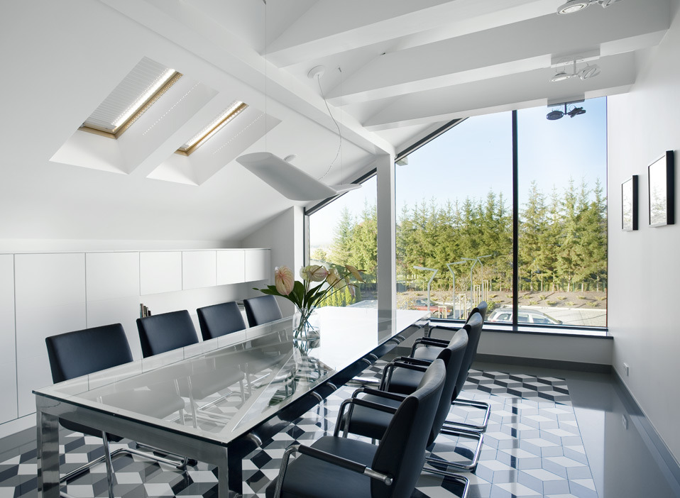 Nowoczesna sala konferencyjna z długim stołem z jasnym blatem, czarnymi krzesłami, wzorzystą podłogą i dużym oknem z widokiem na drzewa.