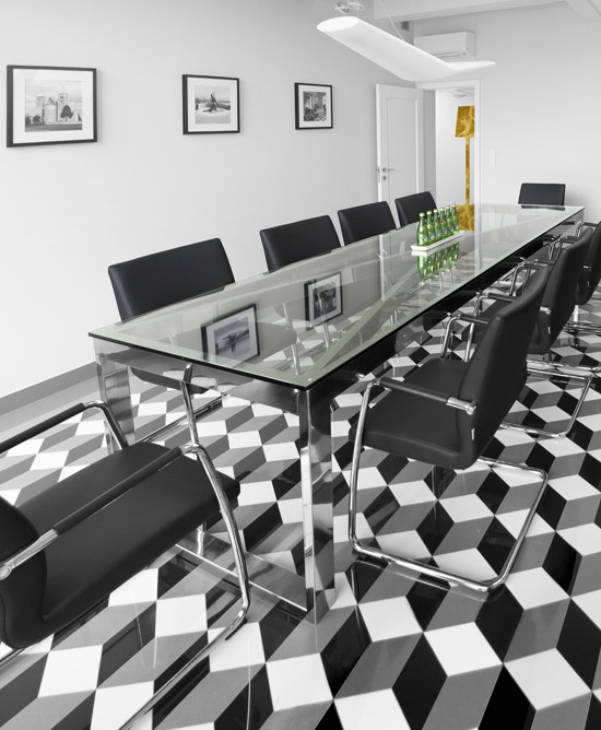 Sala konferencyjna z długim szklanym stołem na chromowanych nogach, czarnymi skórzanymi krzesłami i podłogą w czarno-białe geometryczne wzory 3D