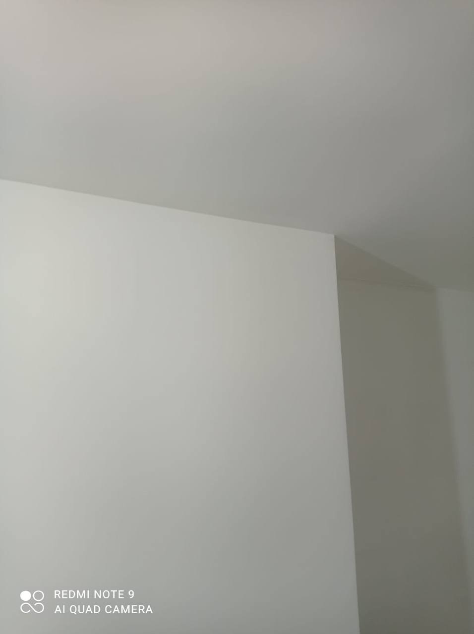 Świeżo pomalowany narożnik pokoju na biało, widoczny fragment sufitu i ściany, oświetlenie z góry tworzy cień na ścianie z prawej strony.