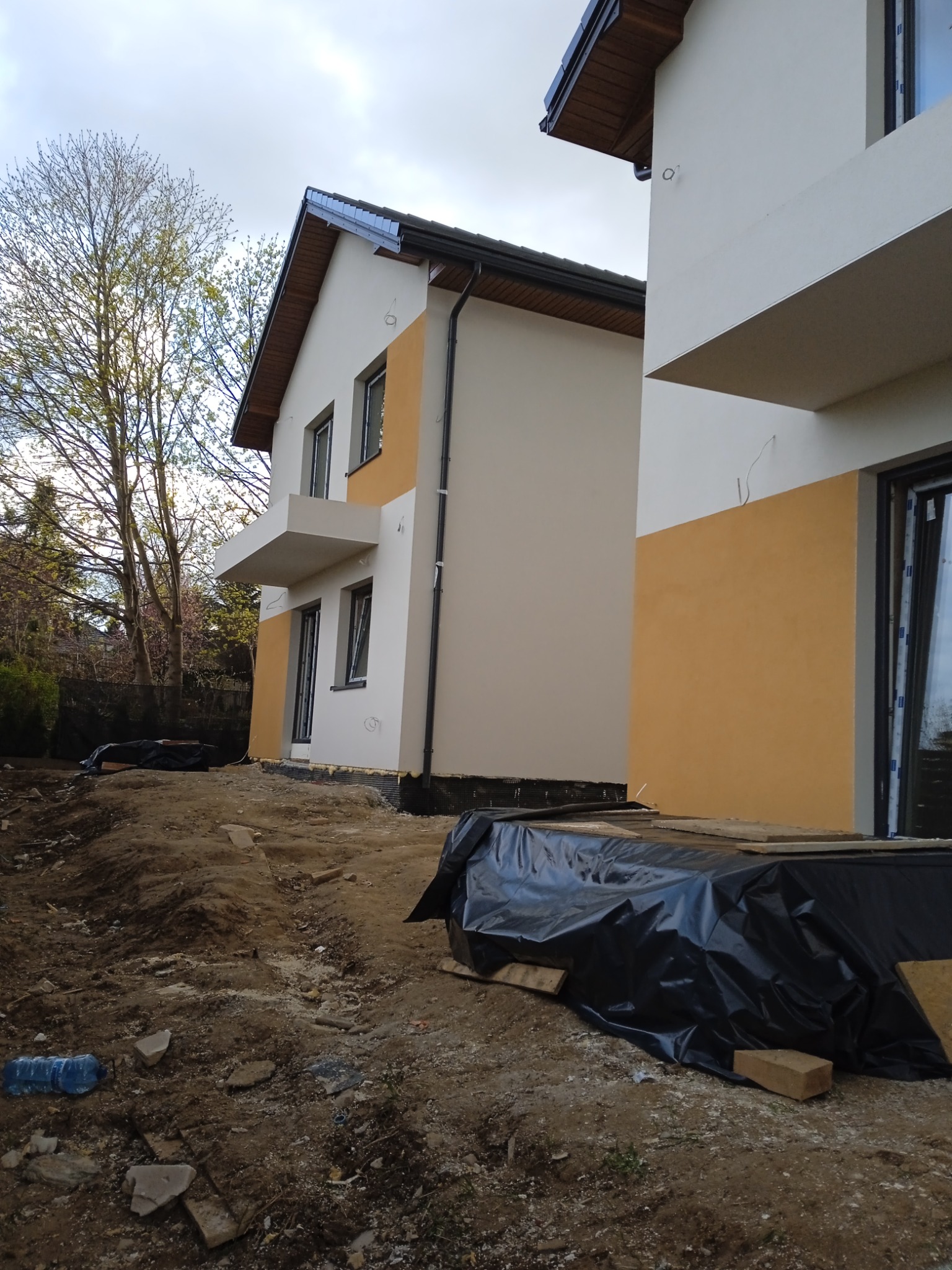 Dwa budynki w Lublinie w trakcie prac wykończeniowych elewacji; fragment ocieplenia widoczny u podstawy ścian, teren wokół zabezpieczony folią.