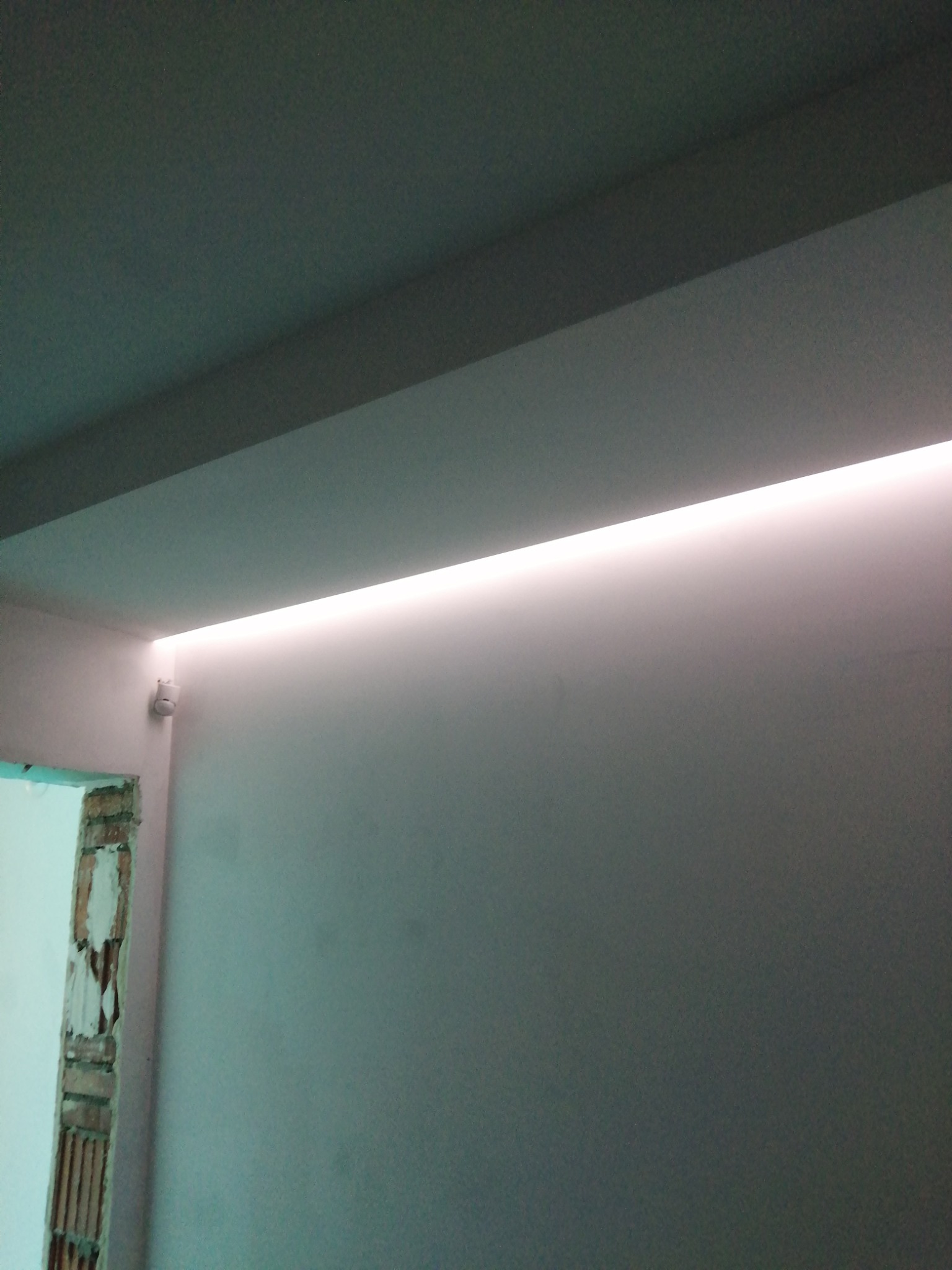 Świeżo pomalowane wnętrze z oświetleniem LED wzdłuż sufitu, widoczne niedokończone obramowanie drzwi.