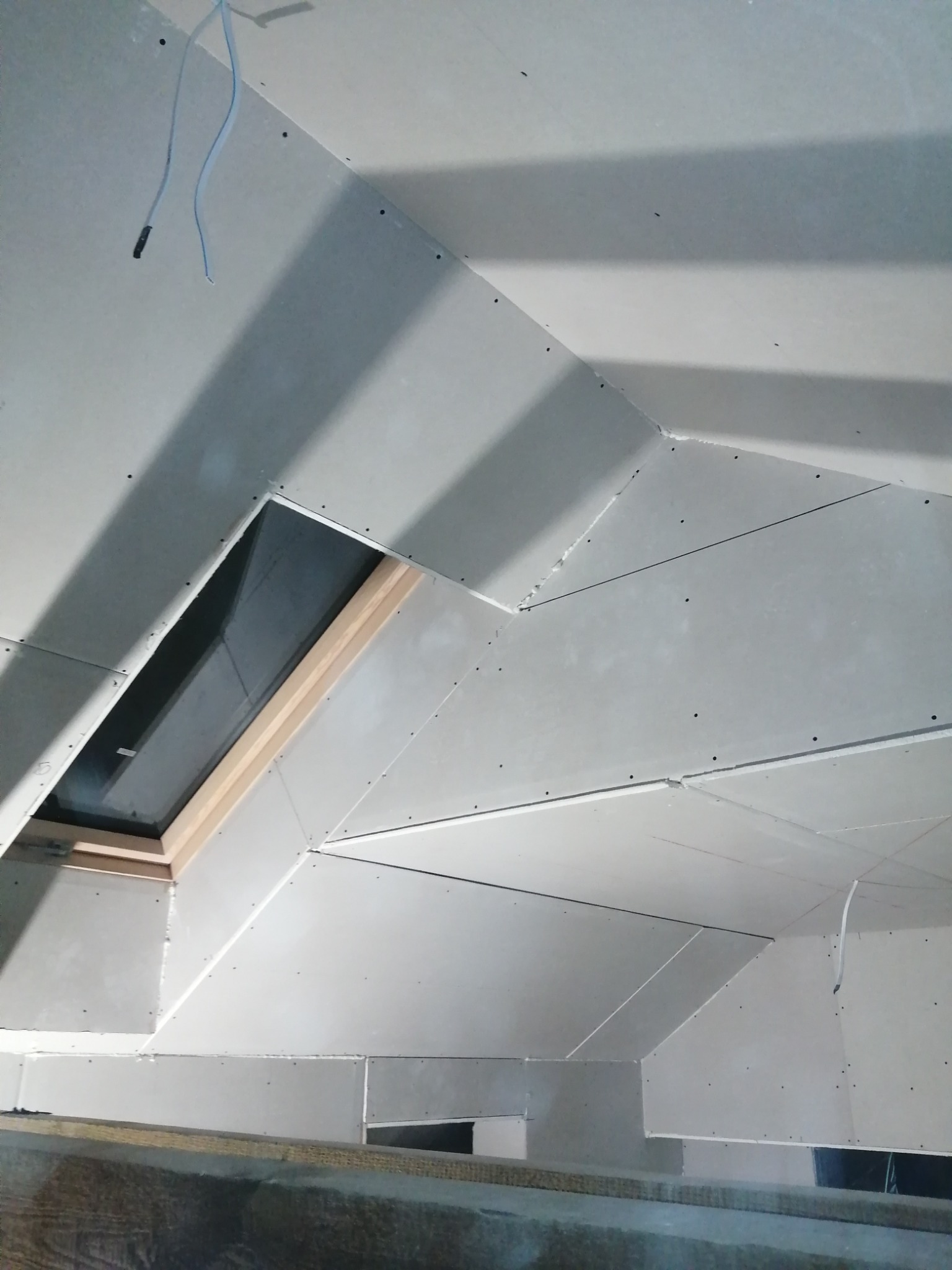 Poddasze z oknem dachowym w trakcie montażu płyt kartonowo-gipsowych, widoczne kable i szpachlowane łączenia.