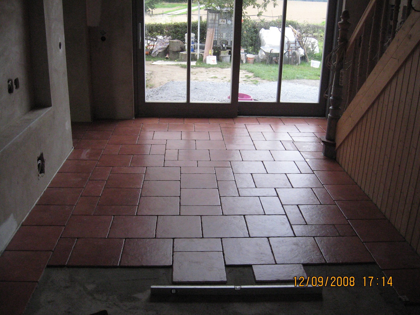 Układanie terakoty w pomieszczeniu z wyjściem na zewnątrz, widoczny poziomica i fragment schodów, ściany w stanie surowym.