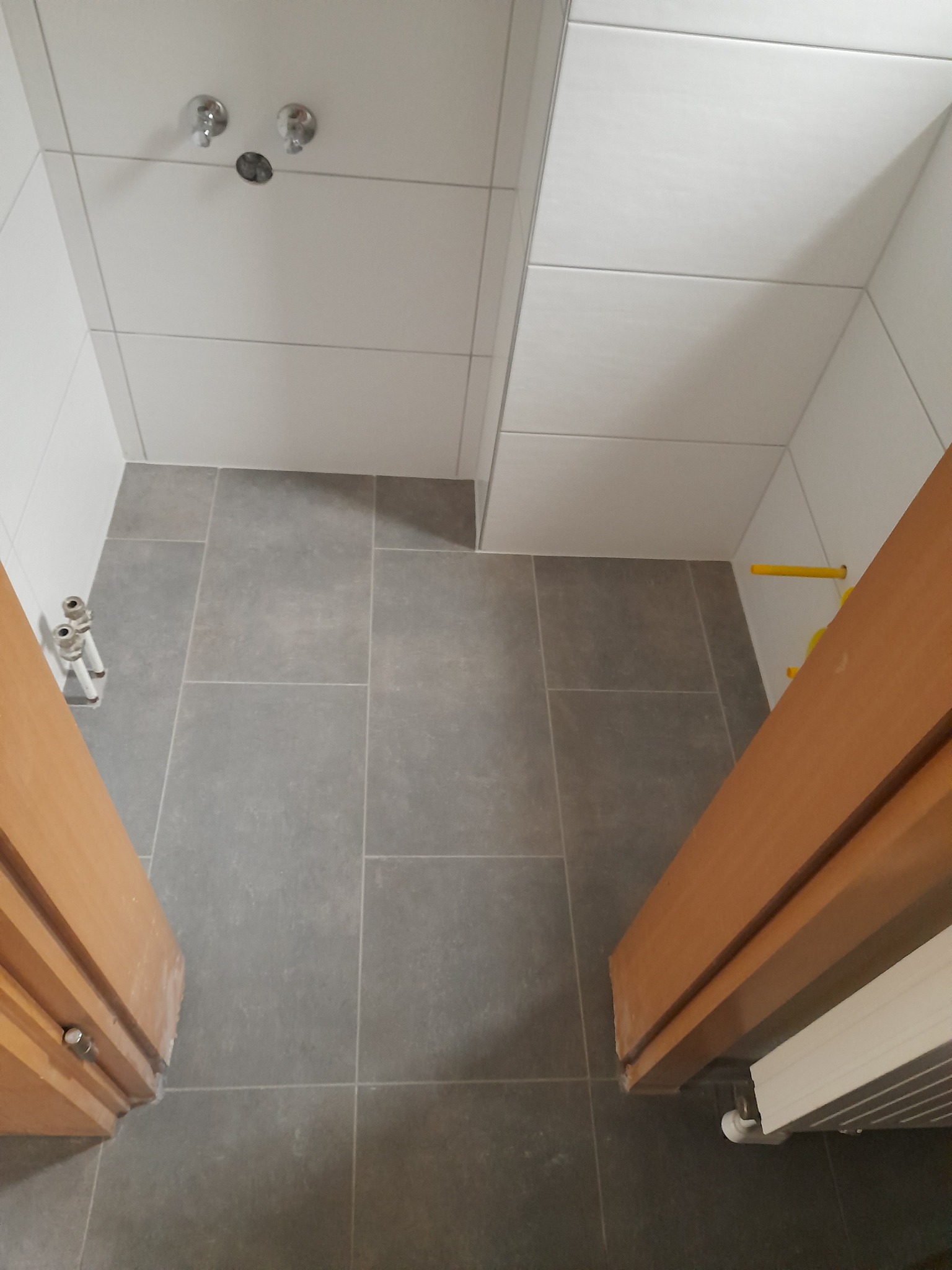 Wykończona łazienka z szarymi płytkami podłogowymi i białymi płytkami ściennymi, widok z góry z elementami instalacji wodnej i grzejnikiem.