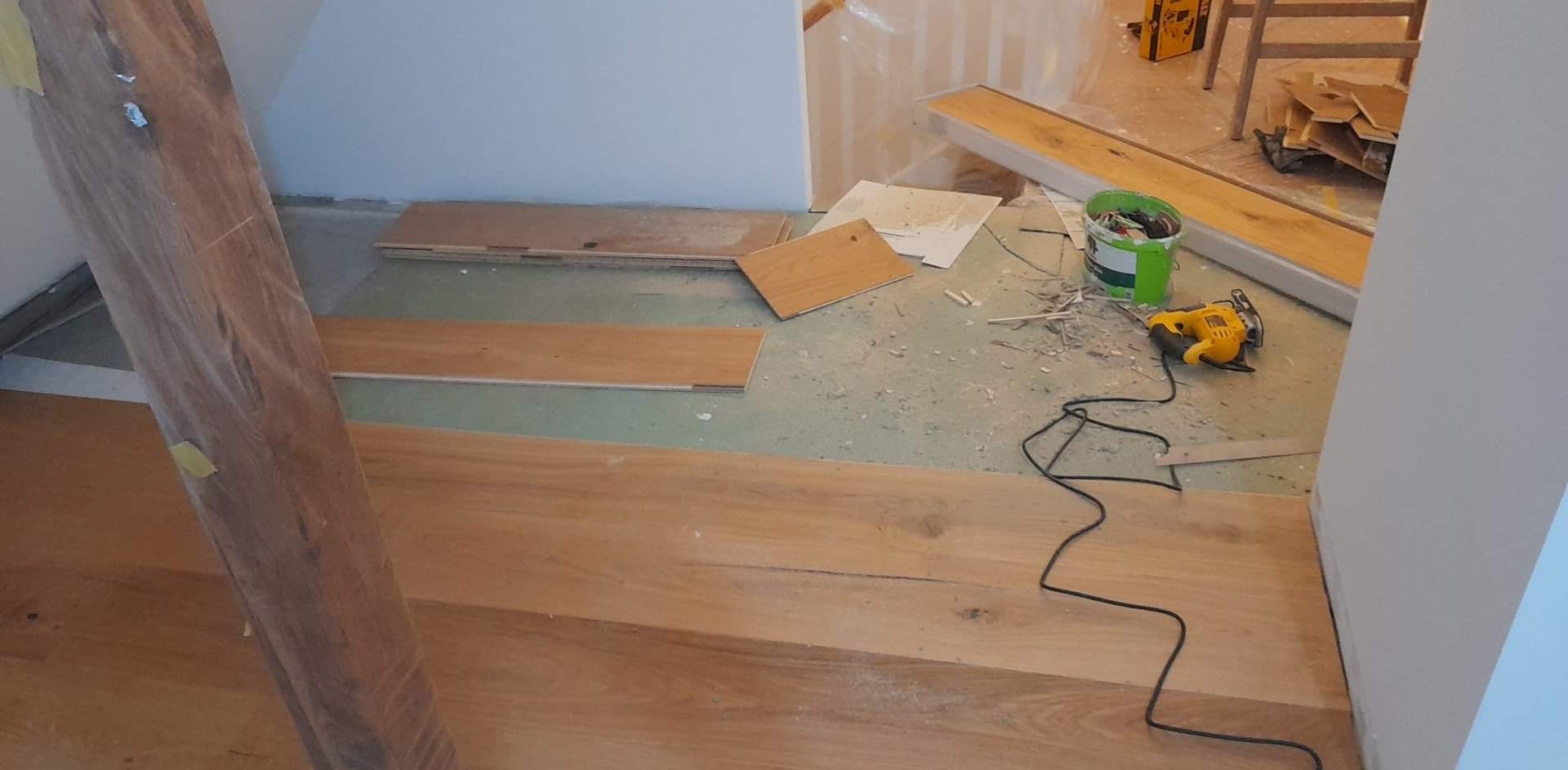 Układanie paneli podłogowych na podkładzie izolacyjnym, widoczna wyrzynarka elektryczna i resztki po cięciu.