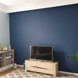 Pomieszczenie po malowaniu ścian na dwa kolory: niebieski i szary, z widocznym telewizorem i elementami dekoracyjnymi na tle ściany w kolorze głębokiego granatu.