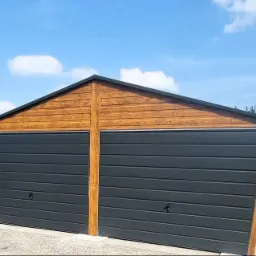 Dwustanowiskowy garaż blaszany z drewnopodobną elewacją i grafitowymi bramami segmentowymi, na tle błękitnego nieba z chmurami.
