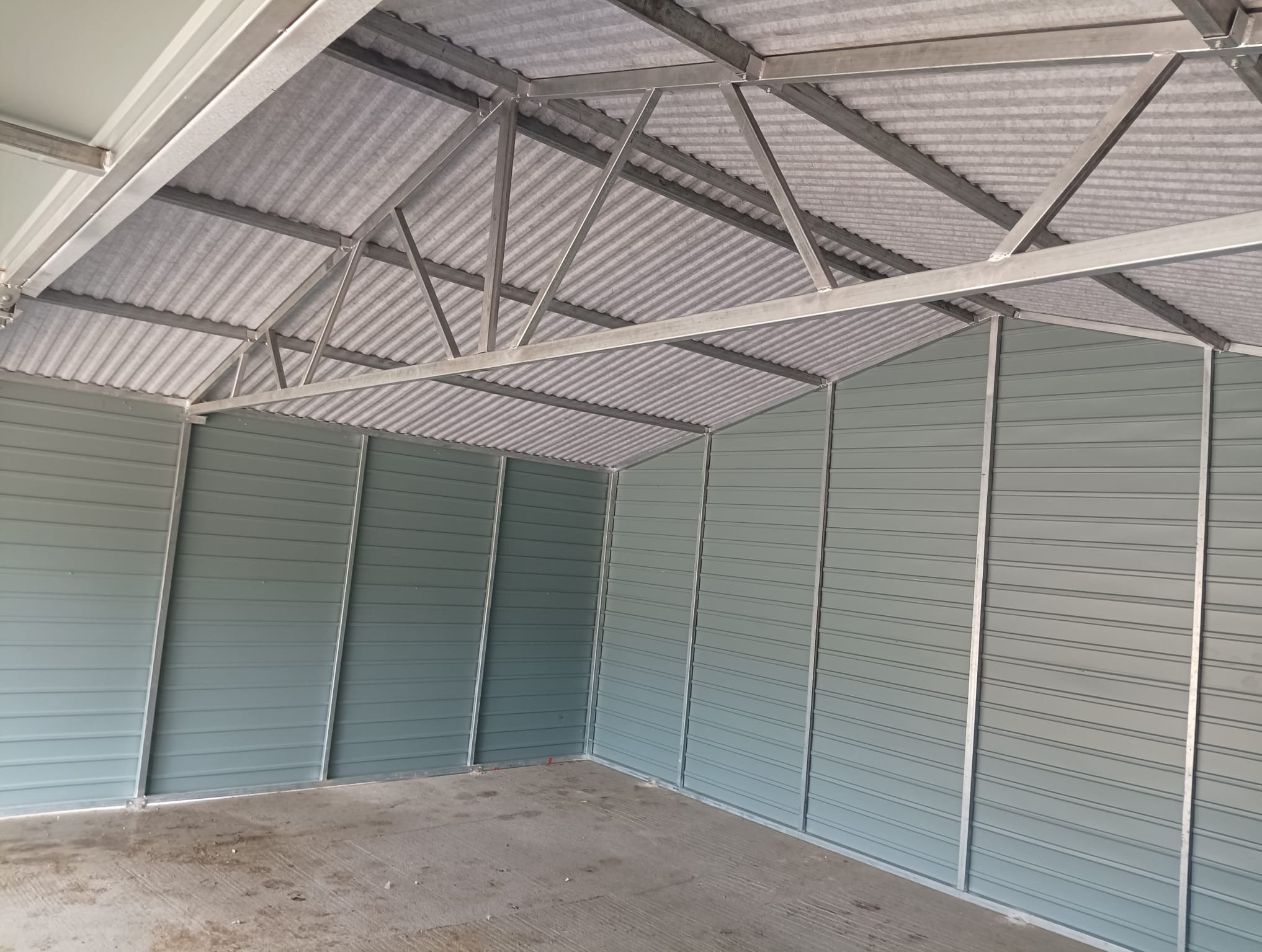 Wnętrze szarego garażu blaszanego z widoczną konstrukcją dachu z metalowych profili i podłogą z betonu.