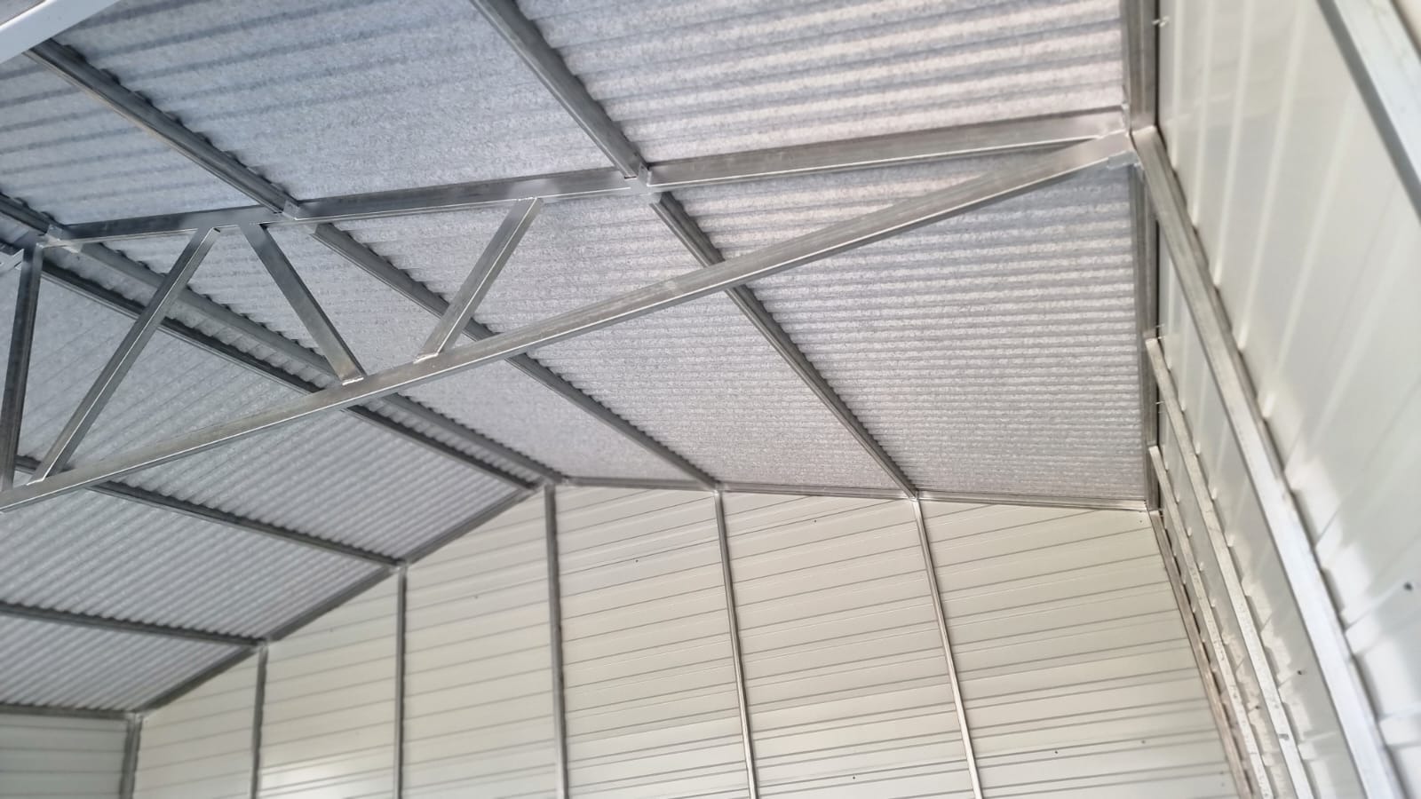 Wnętrze konstrukcji z blachy falistej, widoczne metalowe profile nośne dachu i ścian, surowy stan wykończenia.