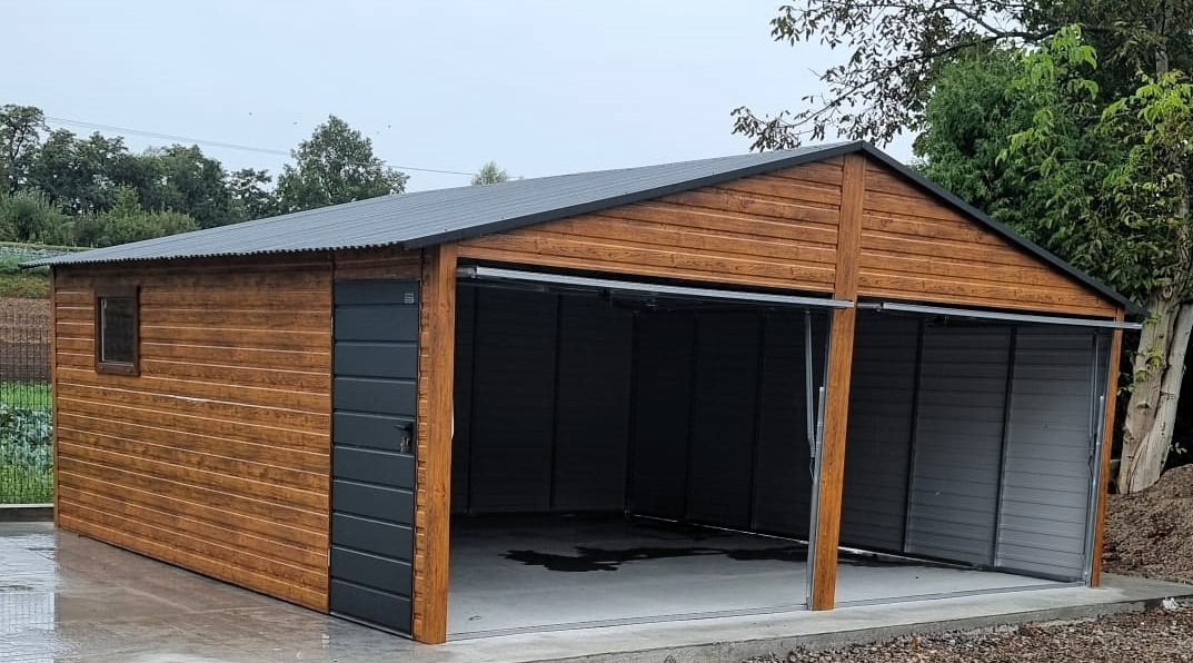 Dwustanowiskowy, drewnopodobny budynek z blachy trapezowej z dwoma otwartymi wrotami, widoczny na tle zieleni.