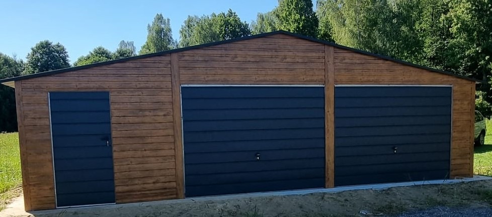 Nowoczesny, drewnopodobny garaż blaszany z dwoma bramami segmentowymi w kolorze grafitowym i drzwiami bocznymi, na tle zieleni.