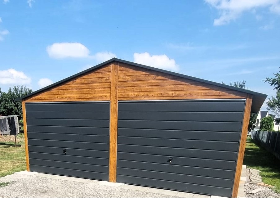 Dwustanowiskowy garaż blaszany z drewnopodobną elewacją i grafitowymi bramami segmentowymi, na tle błękitnego nieba z chmurami.