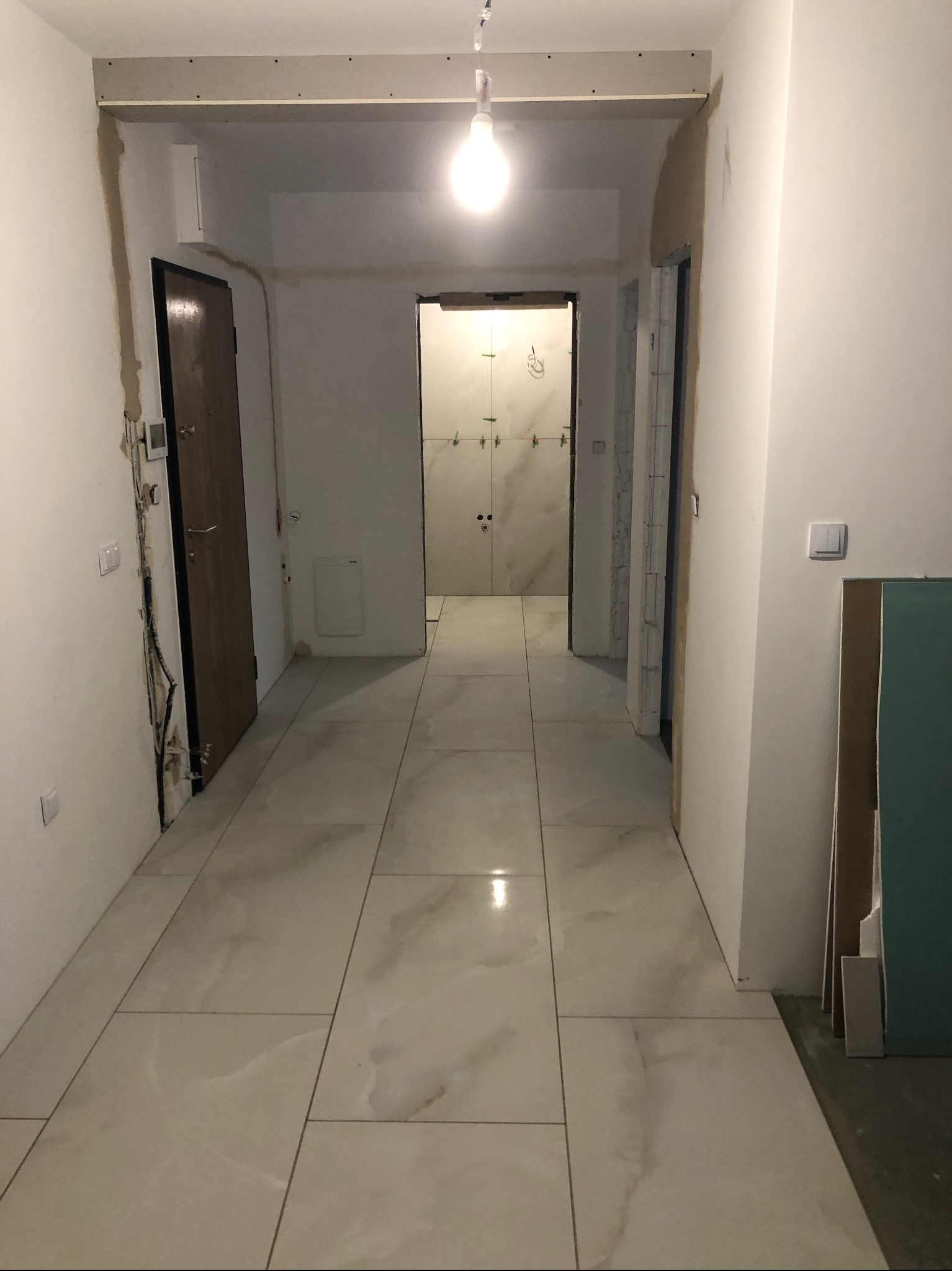 Korytarz w trakcie wykończenia w Zamościu: ułożone płytki podłogowe, przygotowane ściany do malowania, widoczne instalacje elektryczne i sufit podwieszany.
