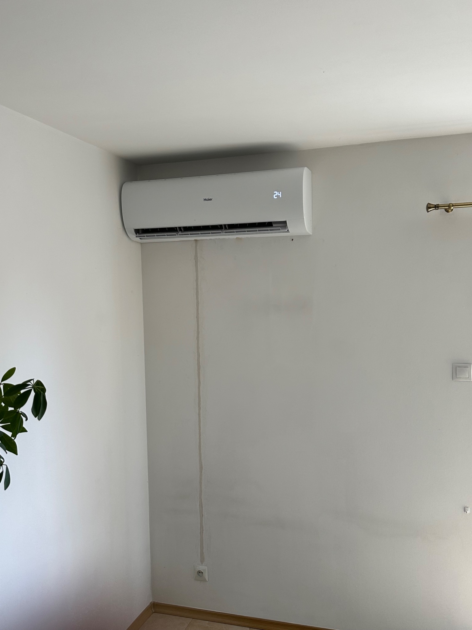 Biały klimatyzator Haier na ścianie w jasnym pomieszczeniu, widoczny ślad po instalacji przewodów, temperatura ustawiona na 24 stopnie.