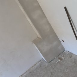 Mateusz Pfeiffer - Szpachlowana wnęka w rogu pokoju, ściany przygotowane do malowania, widoczne ślady po pracy na podłodze.
