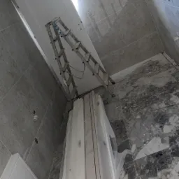 Montaż sufitu podwieszanego w łazience z marmurową podłogą. Widoczna drabina, płyta gipsowa i profile w folii. Ściany wykończone szarą płytką.