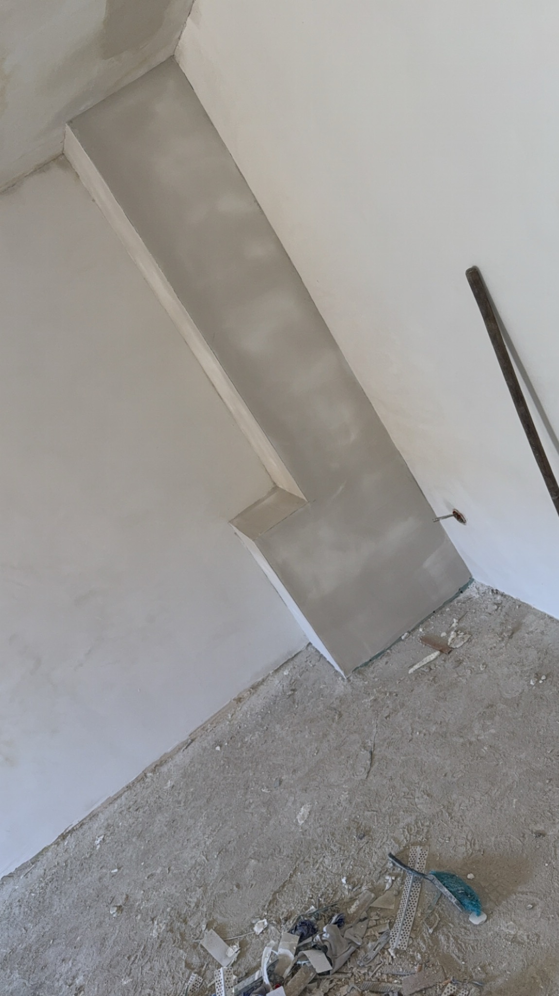 Szpachlowana wnęka w rogu pokoju, ściany przygotowane do malowania, widoczne ślady po pracy na podłodze.