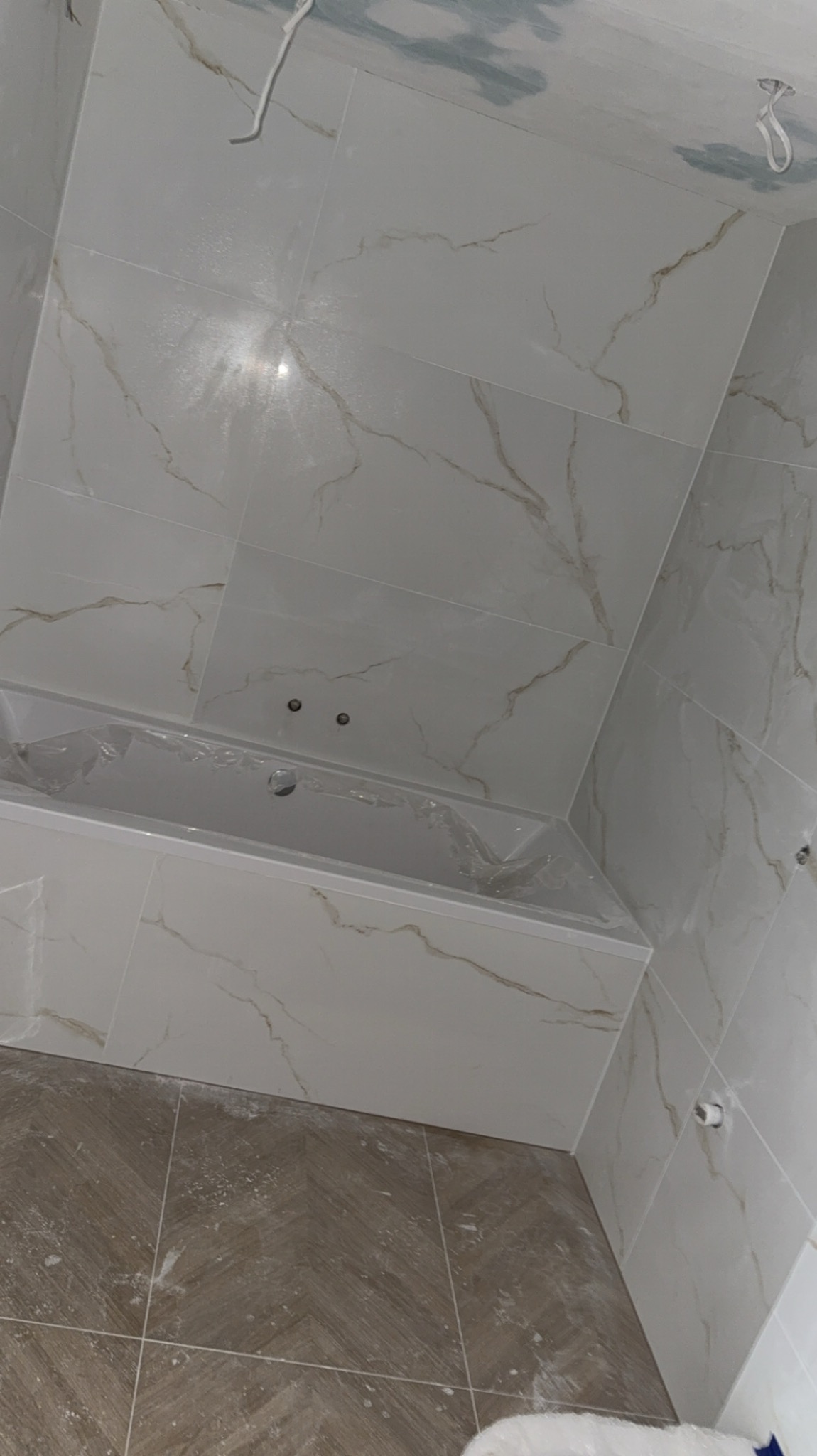 Wykończona łazienka z wanną w zabudowie i marmurkowymi płytkami na ścianach oraz podłodze ułożonej w jodełkę, detale w odcieniach beżu i bieli.