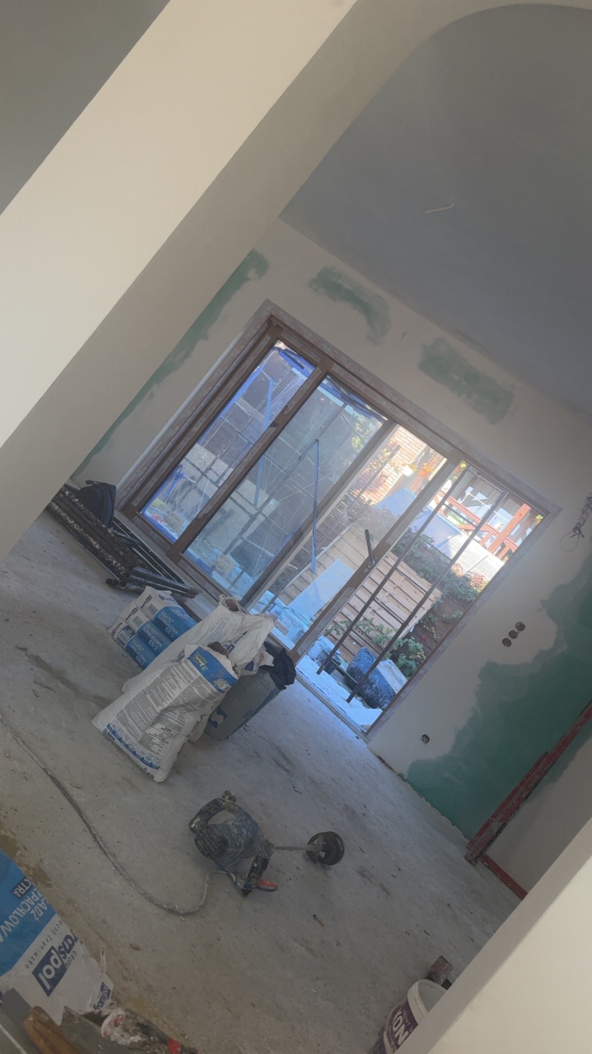 Wnętrze w trakcie szpachlowania: worki z zaprawą, mieszadło do gipsu. Ściany przygotowane pod malowanie, widoczne ślady szpachli. Okno z widokiem na zewnątrz.