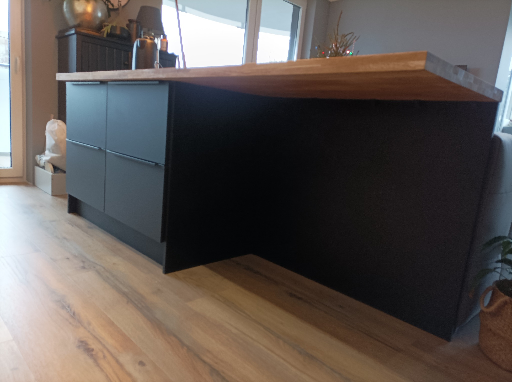 Ciemna wyspa kuchenna z drewnianym blatem, widok z niskiej perspektywy, podkreślający fakturę podłogi i minimalistyczny design.