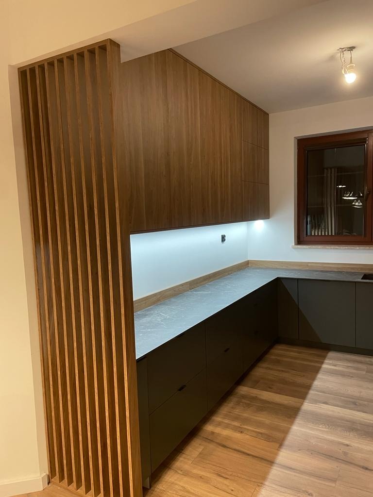 Nowoczesna kuchnia z zabudową meblową w odcieniach szarości i drewna, z drewnianą ścianką działową z pionowych listew i blatem z szarego kamienia