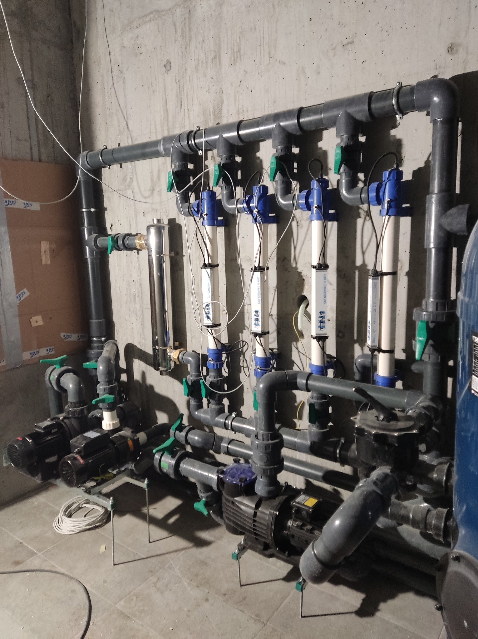 Złożony system rur, zaworów i pomp w Darłowie, prawdopodobnie związany z uzdatnianiem wody, z widocznymi filtrami UV i przewodami elektrycznymi na surowym tle betonowej ściany.