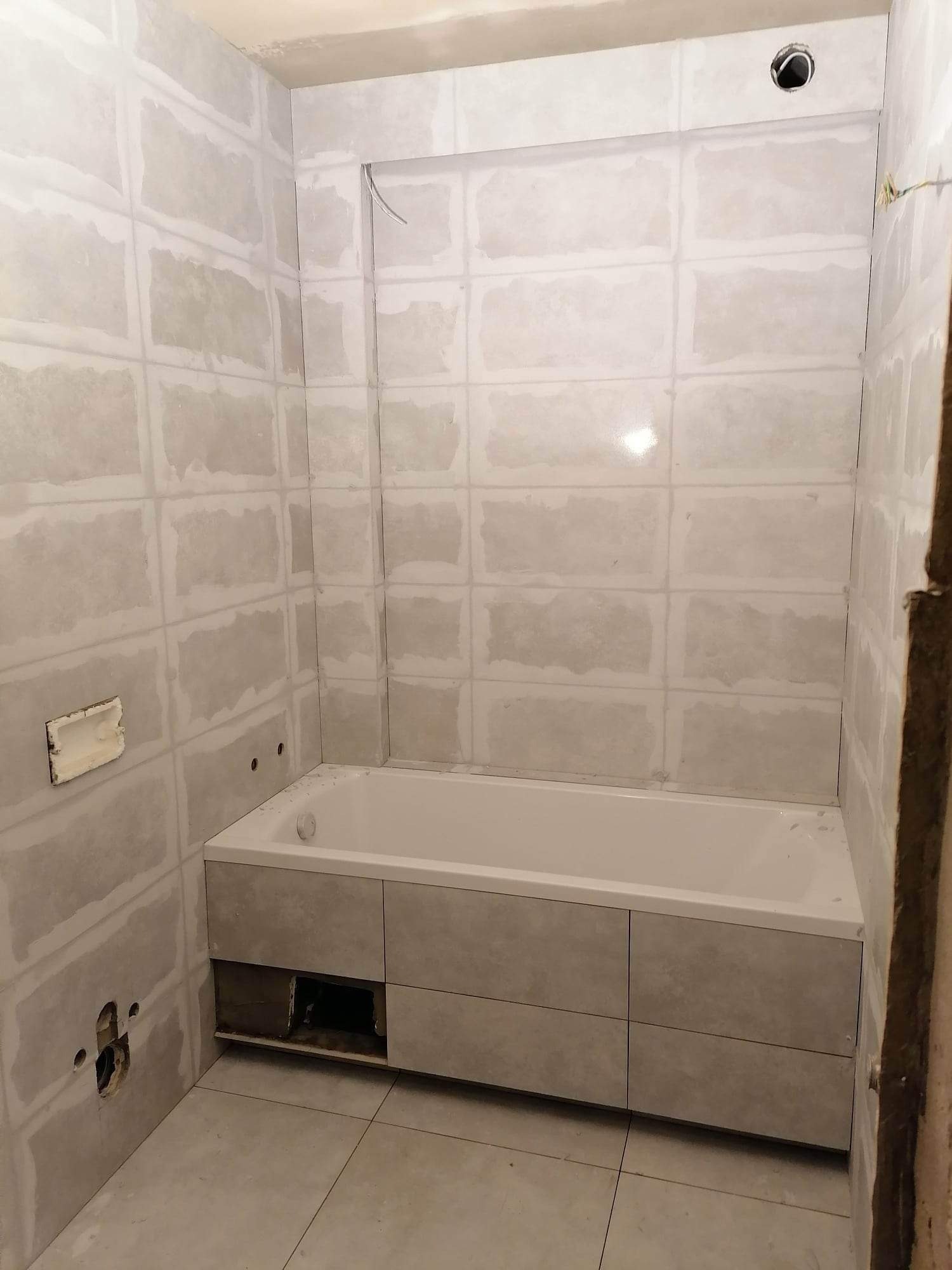 Wanna obudowana płytami w trakcie prac wykończeniowych w łazience, ściany przygotowane pod płytki, widoczne otwory na instalacje.