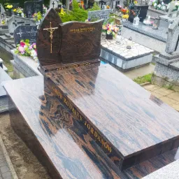 Dwupoziomowy, brązowo-czarny nagrobek z granitu z napisem 'Grób Rodziny Jordanów' na cmentarzu, z krzyżem z wizerunkiem Chrystusa na pionowej płycie.