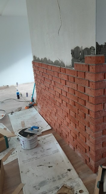 Montaż dekoracyjnej ściany z cegieł w surowym stanie, widoczne narzędzia i materiały budowlane, fragment ściany przygotowany pod dalsze prace.