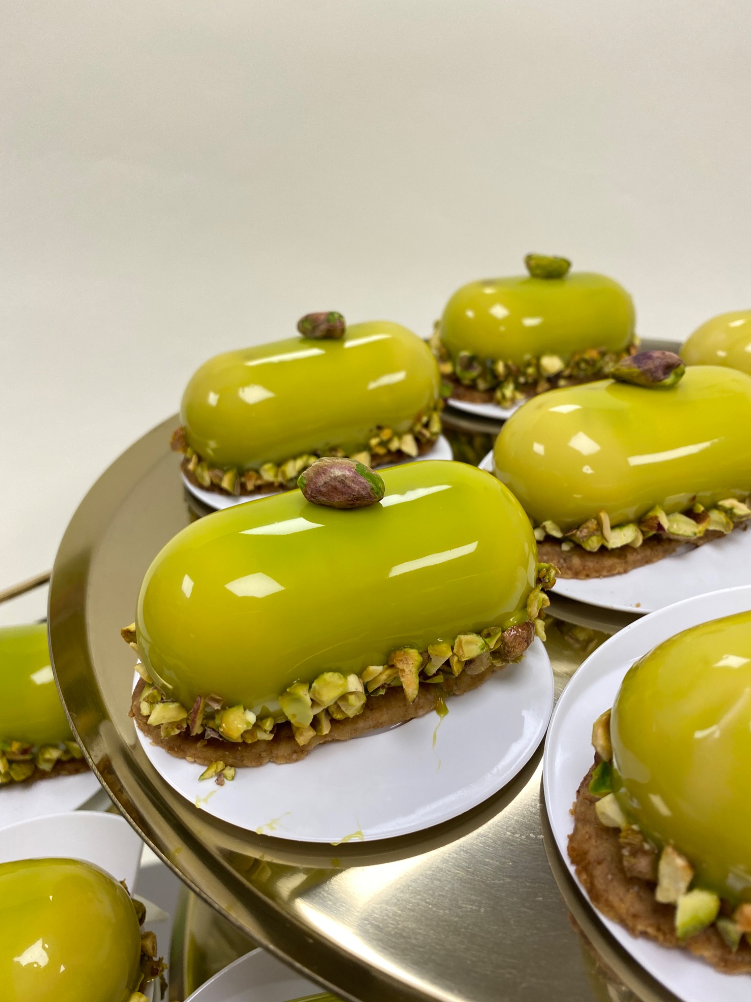 Pistacjowe mini-desery z lustrzaną polewą i posiekanymi pistacjami na złotym etażerze.