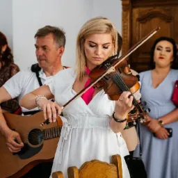 Kwartet muzyczny w trakcie występu w Kielcach: blondwłosa skrzypaczka w białej sukience, gitarzysta i dwie kobiety w tle.