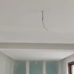 Wnętrze w trakcie prac wykończeniowych: sufit z podwieszaną konstrukcją, ściany częściowo pokryte płytami gipsowo-kartonowymi, widoczne przewody elektryczne