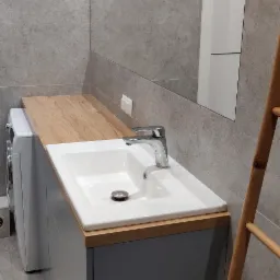 Nowoczesna łazienka z szarą zabudową umywalki z drewnianym blatem, białą umywalką, chromowaną baterią i drabinką dekoracyjną z bambusa.