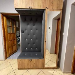 Produkcja i sprzedaż mebli Tomasz Dynus - Drewniana zabudowa przedpokoju z tapicerowanym siedziskiem, wieszakami i lustrem, widok na otwarte drzwi do kuchni.