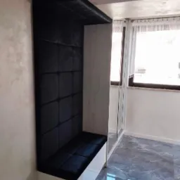 Wnęka z siedziskiem obita czarnym, pikowanym welurem, wkomponowana w białą szafę z lustrzanymi drzwiami, na tle marmurowej podłogi.