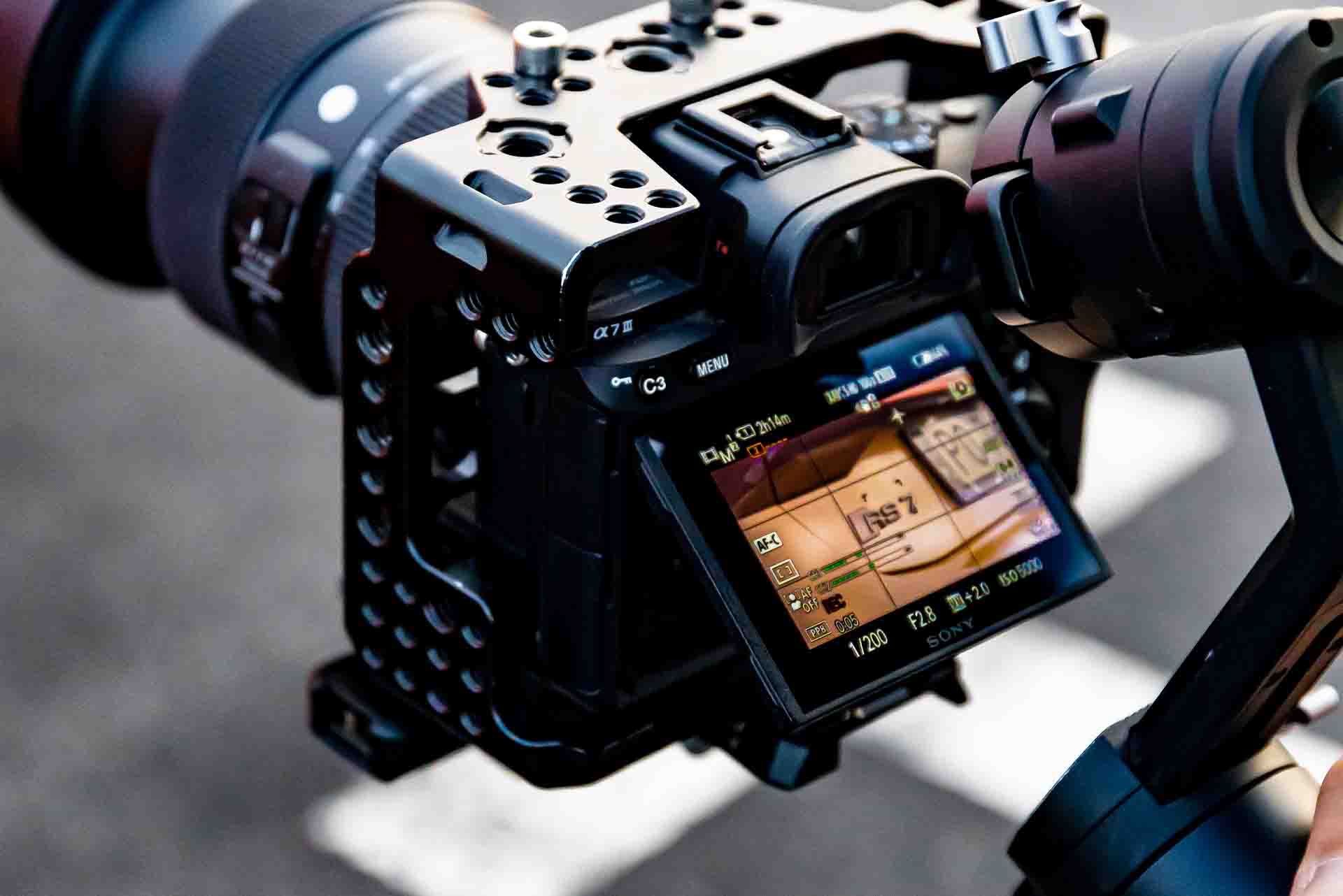 Profesjonalna kamera Sony Alpha 7 z obiektywem Sigma i stabilizatorem, ustawiona na nagrywanie wideo, widoczny ekran z podglądem kadru i ustawieniami ekspozycji.