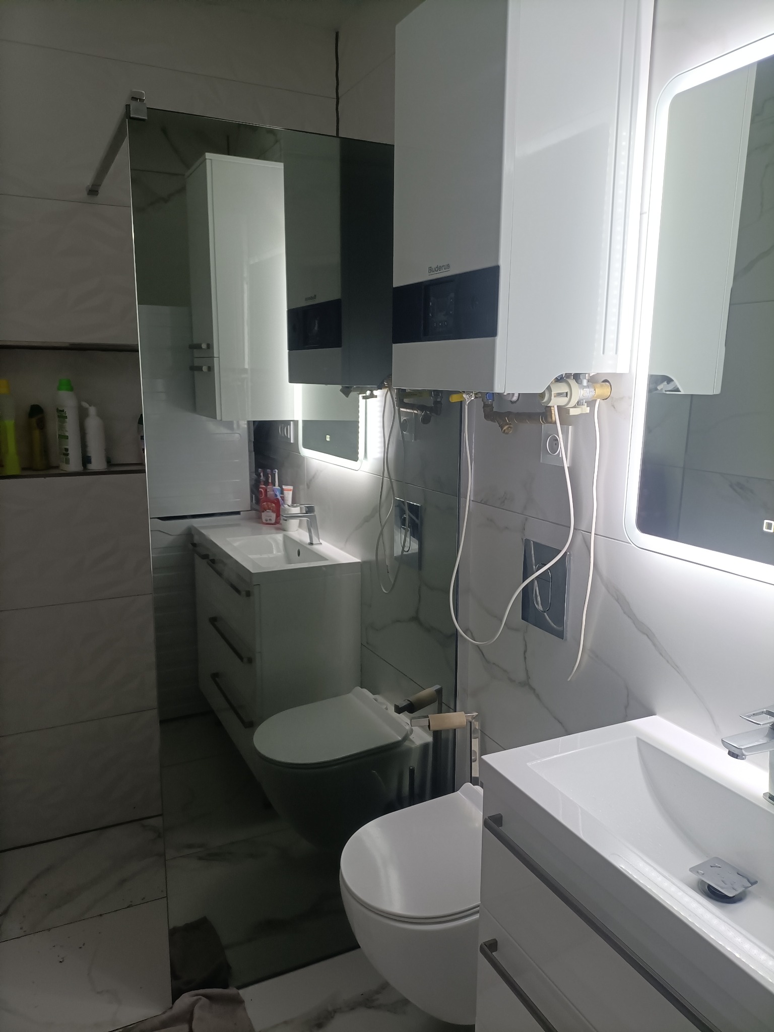 Nowoczesna łazienka z zamontowanym piecem gazowym Buderus, widoczne rury i elementy instalacji, marmurowe płytki na ścianach.