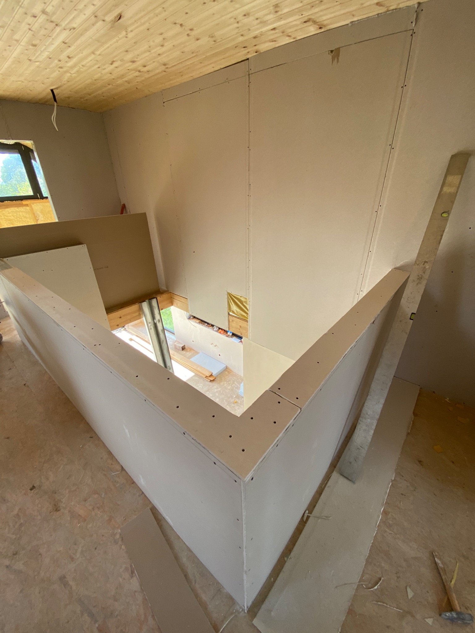 Montaż ścianki działowej z płyty karton gips na poddaszu z drewnianą boazerią sufitową, widoczny poziomica przy ścianie i narzędzia na podłodze.