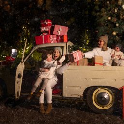 www.fotokutkowska.pl - Świąteczna sesja rodzinna przy starym samochodzie z prezentami i skrzynką na listy do Mikołaja, w tle oświetlone choinki i padający śnieg.